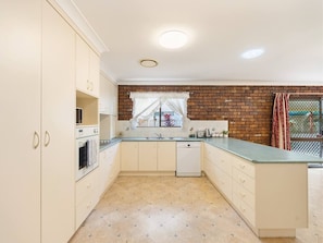 A kitchen with white cabinets, a brick backsplash, a window with curtains, and a dishwasher. - Affordable Stay | Near Sunnybank |Prime Location (Robertson)