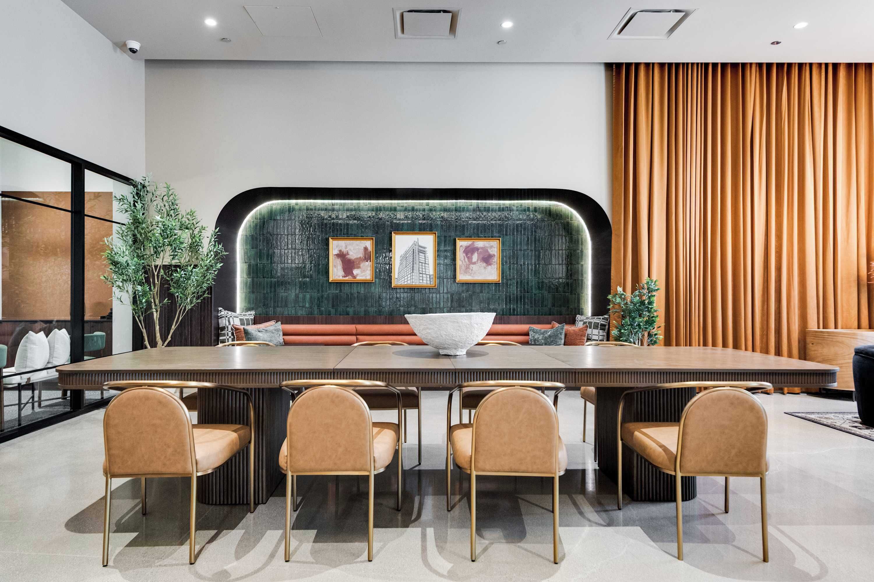 Une salle de conférence moderne, dotée d’une longue table, de six chaises, d’un mur texturé de couleur verte et d’œuvres d’art encadrées.