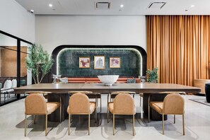 A modern conference room with a long table, six chairs, a green textured wall, and framed artwork.