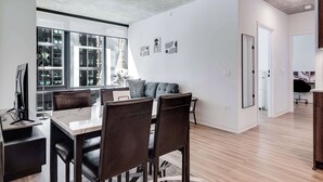 A modern living room with a dining area, large windows, and a view of the city. - Wabash 4BR - Pool, Free In & Out Parking 1 (Chicago)