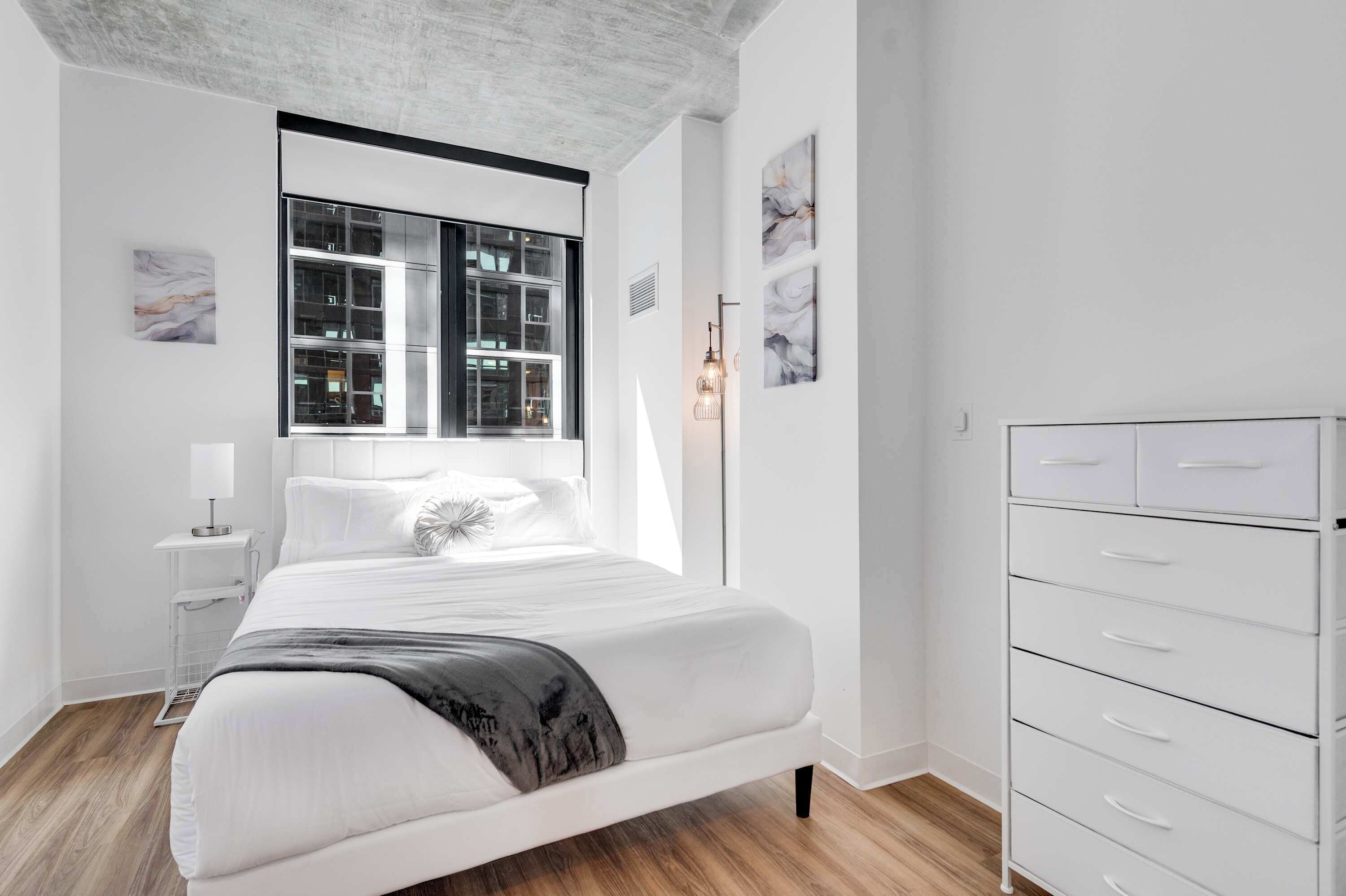Quarto moderno com cama grande, mesa de cabeceira, abajur e guarda-roupa.