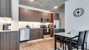 A modern kitchen with wooden cabinets, a microwave, oven, and a refrigerator. There is a dining table with chairs and a clock on the wall. - Wabash 4BR - Pool, Free In & Out Parking 1 (Chicago)