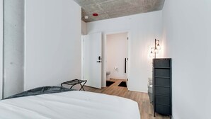 A modern bedroom with a bed, a black metal drying rack, a wardrobe, and a bathroom visible through an open door. - Wabash 4BR - Pool, Free In & Out Parking 1 (Chicago)