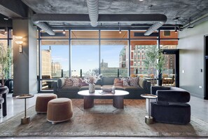A modern lounge area with a large window, a sofa, ottomans, and a coffee table.