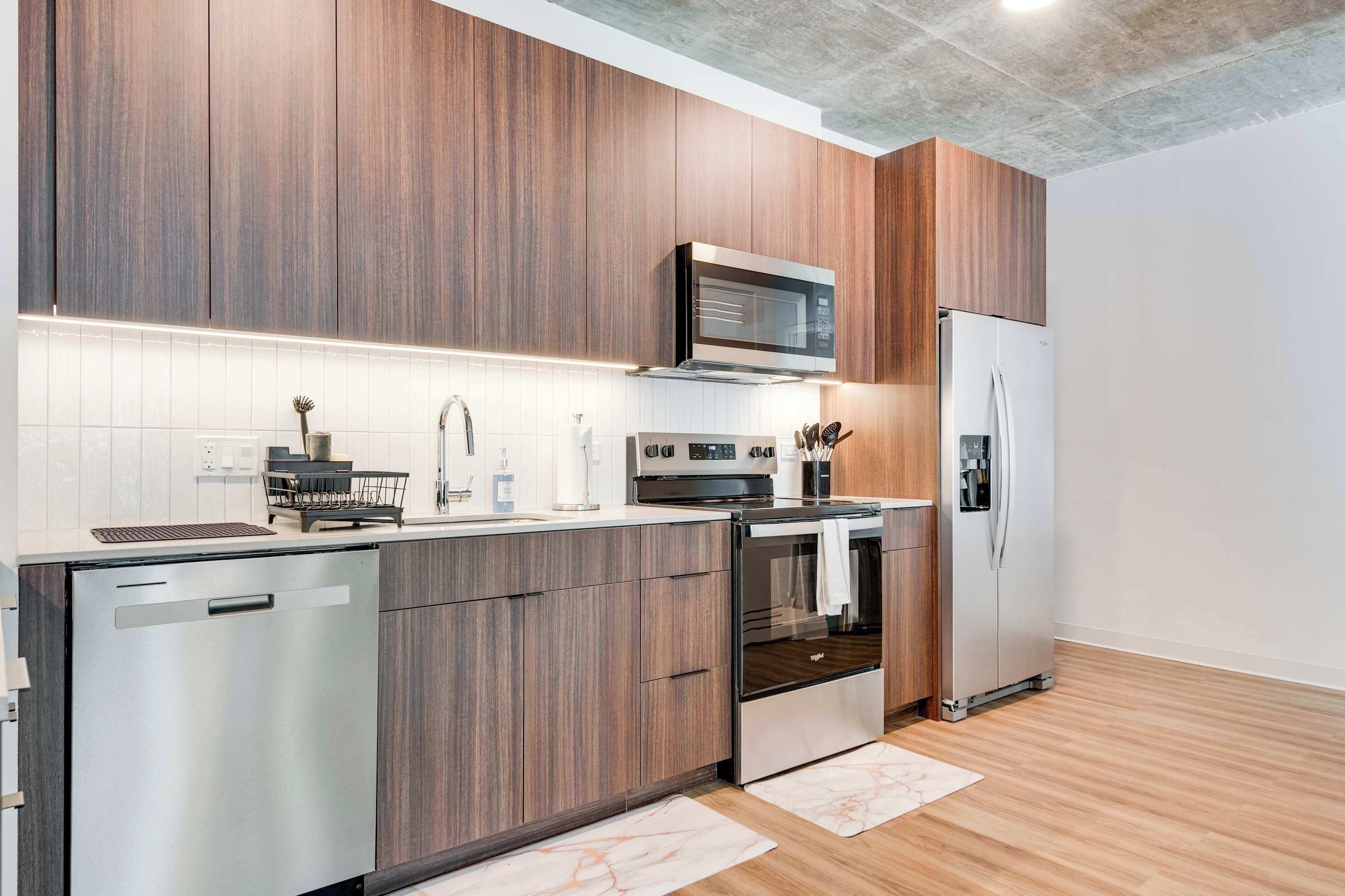 Une cuisine moderne avec des meubles en bois, des appareils en acier inoxydable et un dosseret de carrelage blanc.