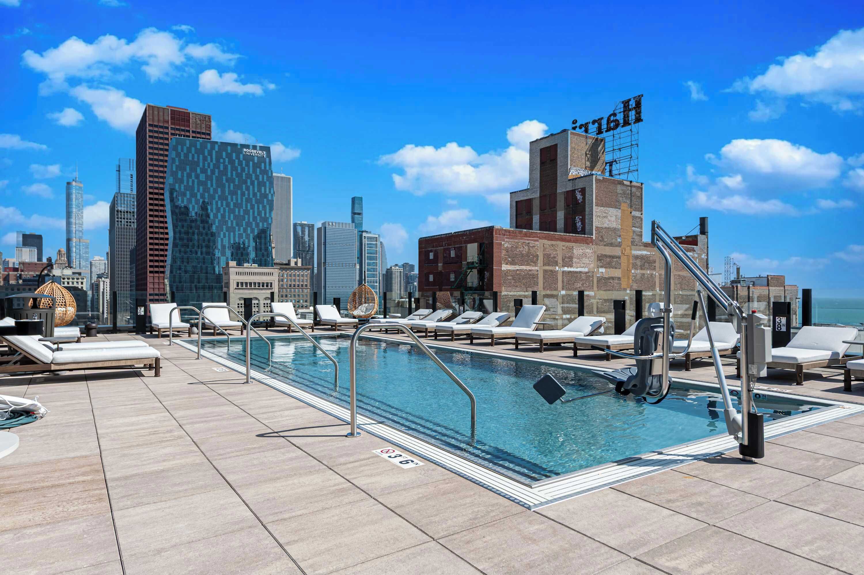 Piscina no terraço com espreguiçadeiras e paisagem urbana ao fundo.