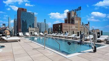 Piscina no terraço com espreguiçadeiras e paisagem urbana ao fundo.