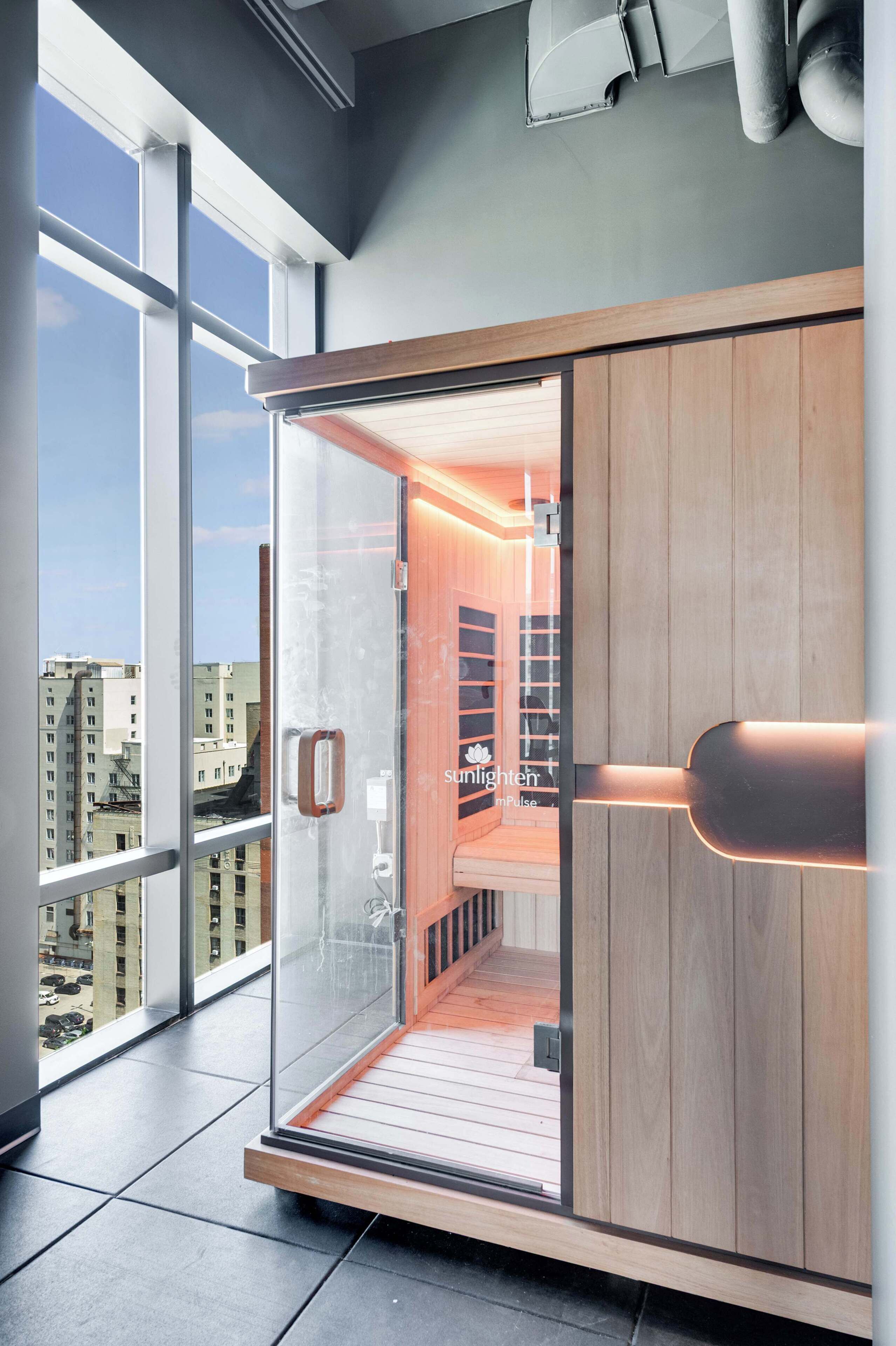 Une chambre moderne dotée d’une porte en verre donnant sur un espace sauna en bois, de grandes fenêtres et offrant une vue sur la ville.