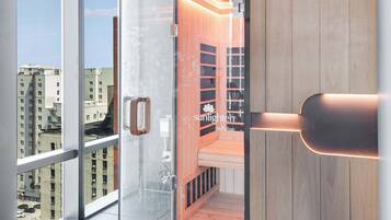 Une chambre moderne dotée d’une porte en verre donnant sur un espace sauna en bois, de grandes fenêtres et offrant une vue sur la ville.