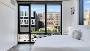 A modern hotel room with a large bed, a view of city buildings, and a large window. - Wabash 4BR - Pool, Free In & Out Parking 2 (Chicago)