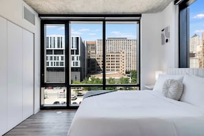 Una moderna camera d'hotel con un letto grande, vista sugli edifici della città e un'ampia finestra.