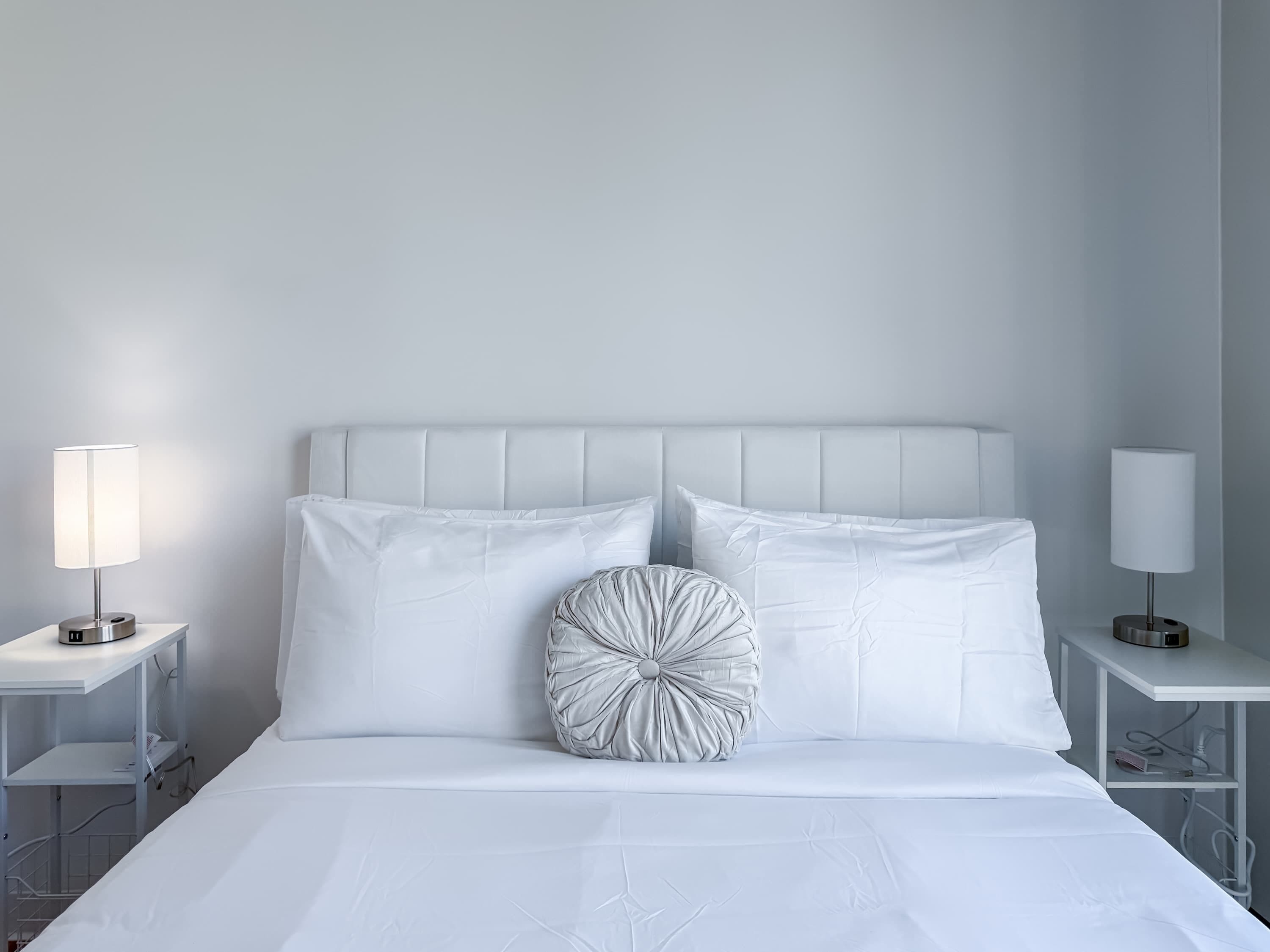 A neatly made bed with white bedding, two bedside tables with lamps, and a single decorative pillow.