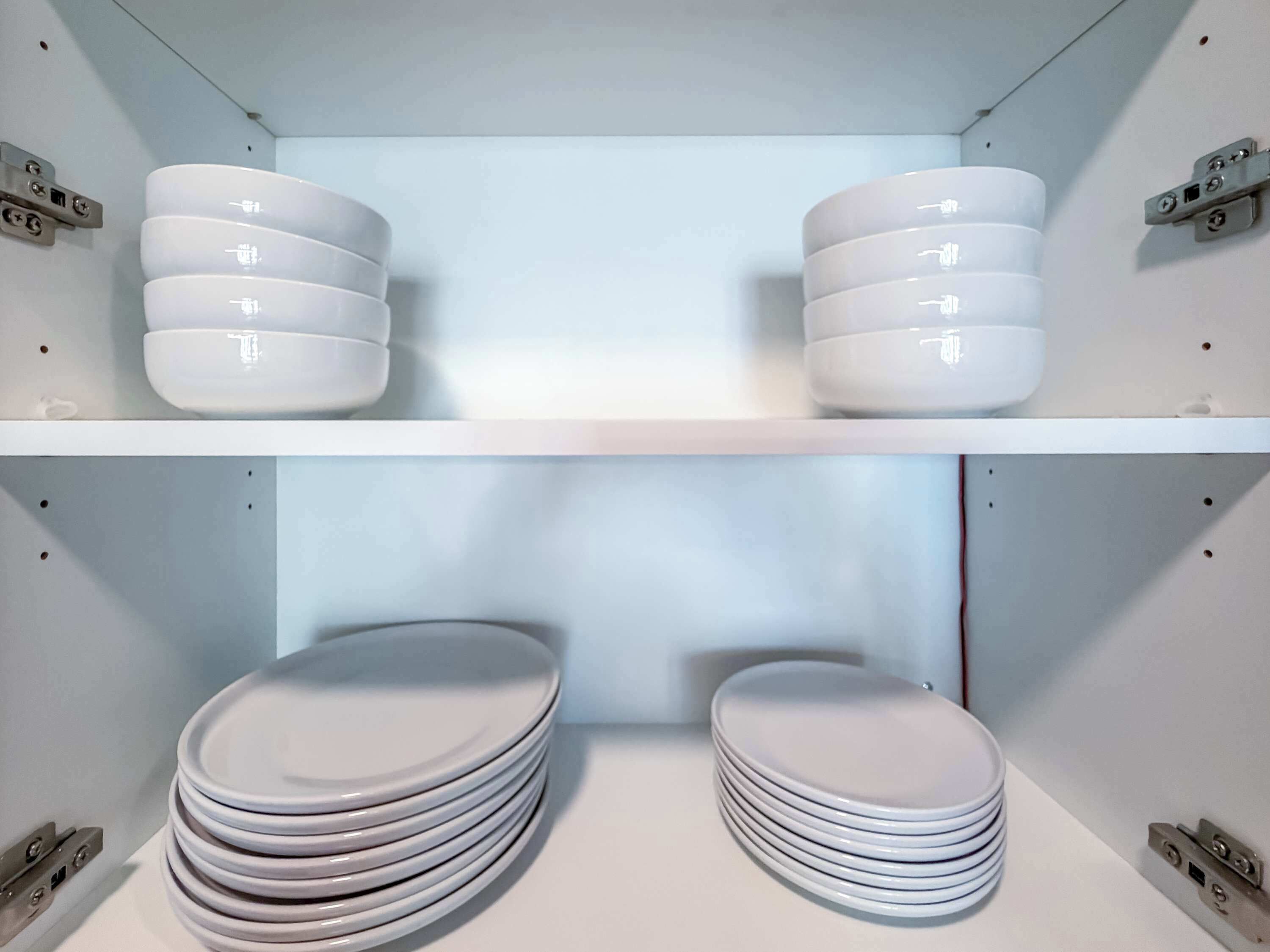 Un baño con dos estantes blancos, uno encima del otro, cada uno sosteniendo una pila de platos blancos.