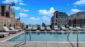 Piscina no terraço com espreguiçadeiras e vista para a paisagem urbana.