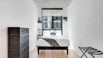 A modern bedroom with a bed, a dresser, a lamp, and a view of the outside.