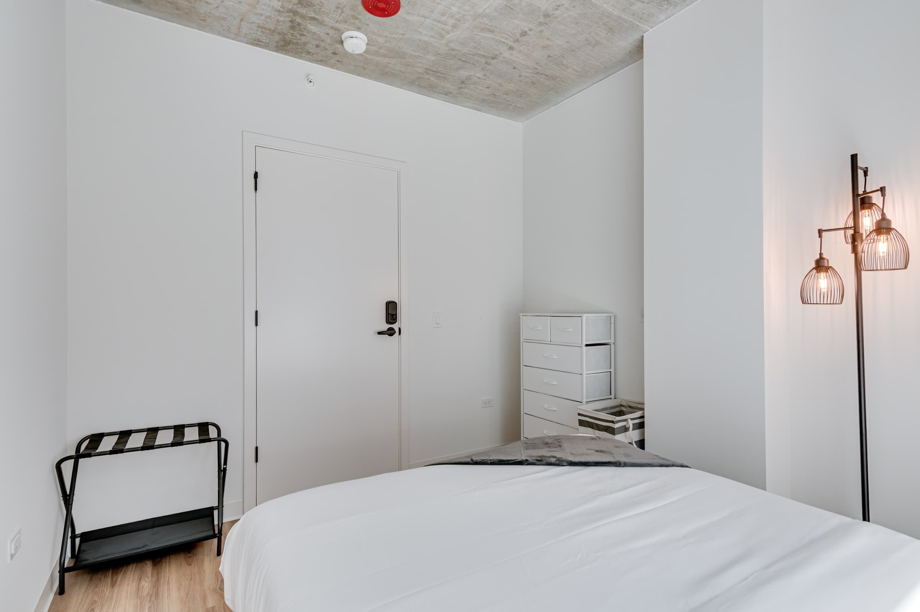 Quarto com cama, guarda-roupa, um banco e uma luminária de chão.