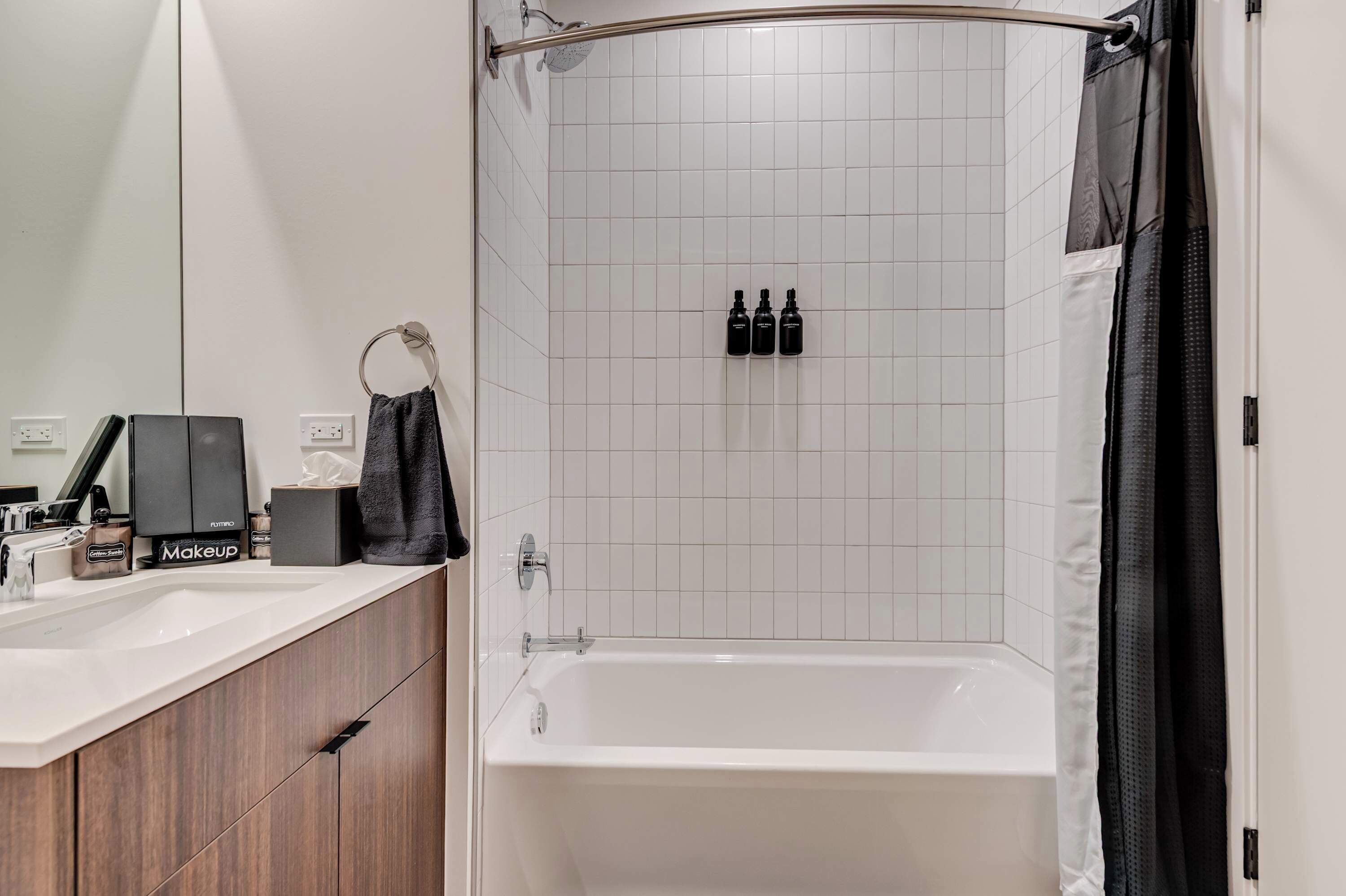 Uma casa de banho moderna com chuveiro em azulejos brancos, uma banheira e um lavatório com espelho e produtos de higiene pessoal.