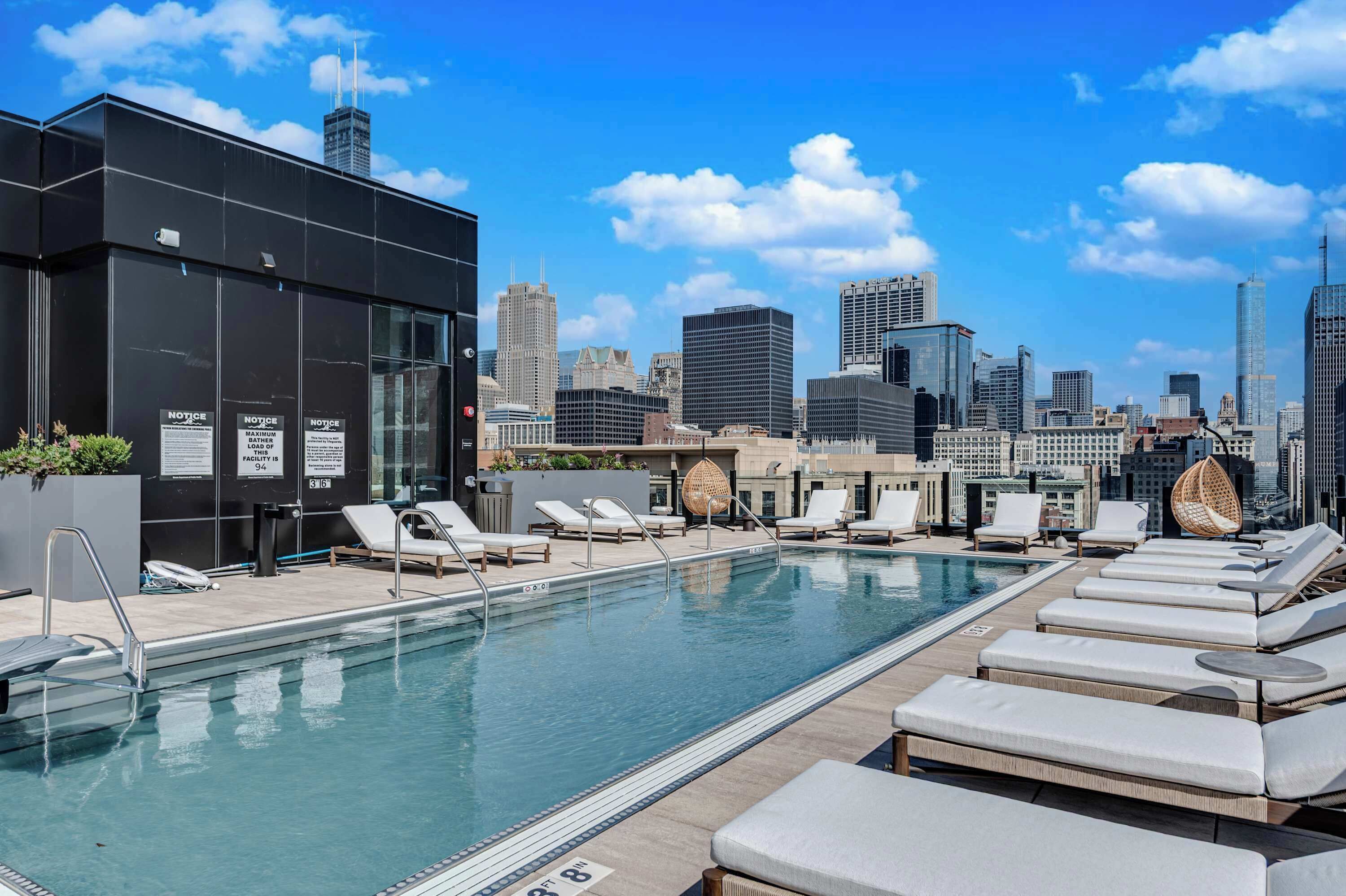A rooftop pool with lounge chairs and a city skyline in the background.
