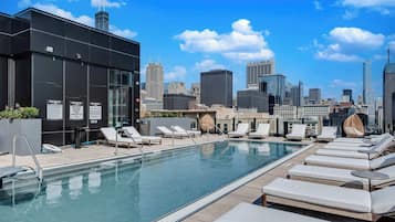 A rooftop pool with lounge chairs and a city skyline in the background.