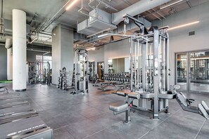 A modern gym with various weightlifting equipment, a mirror wall, and a view of the city through large windows. - Wabash 4BR - Pool, Free In & Out Parking 4 (Chicago)