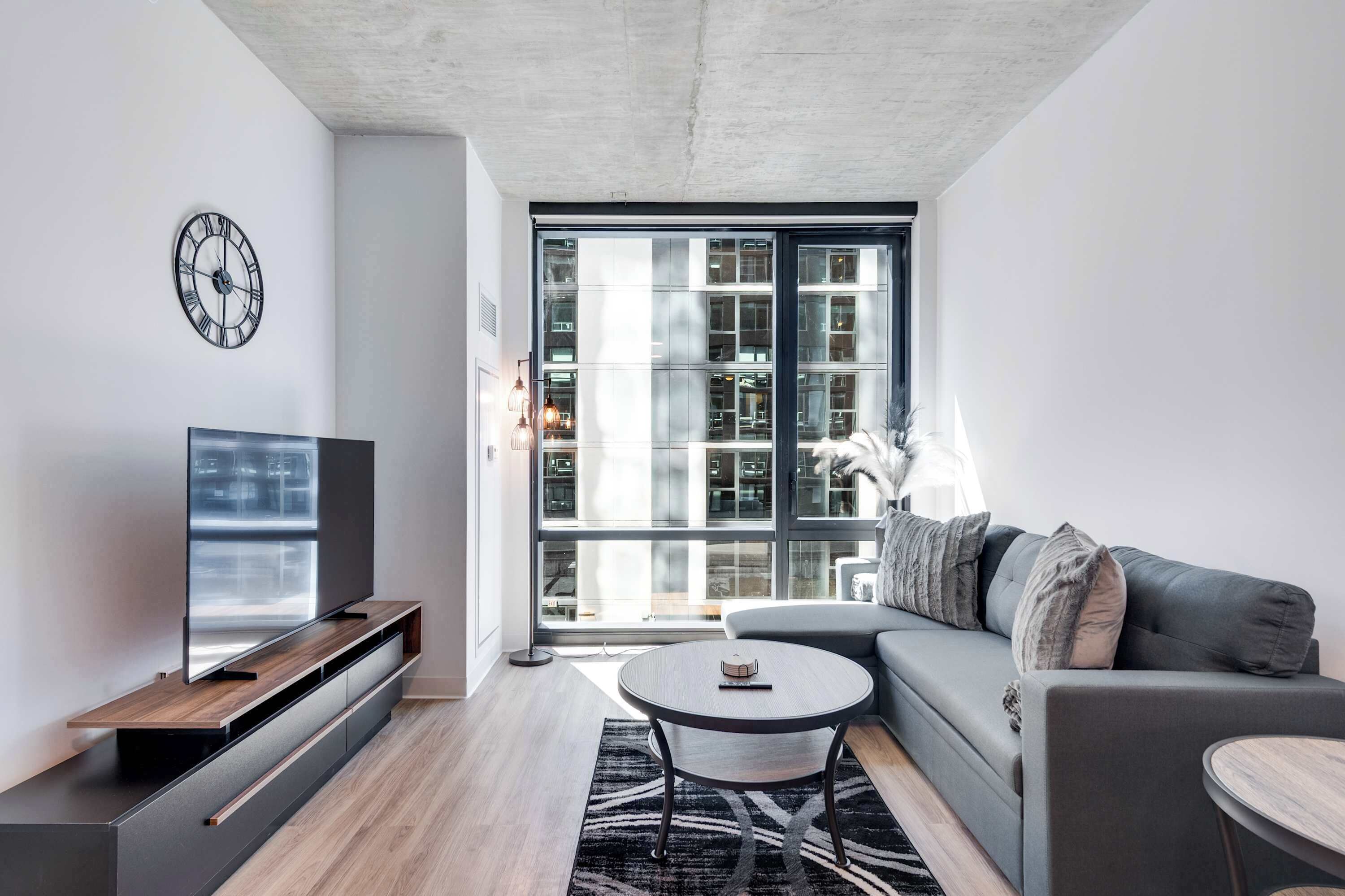 A modern living room with a flat-screen TV, a sofa, a coffee table, and a large window with a view of a building.
