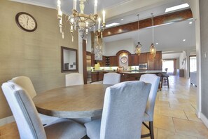 Un vaste espace dédié à la salle à manger, avec une table et des chaises en bois, un lustre et une horloge au mur.