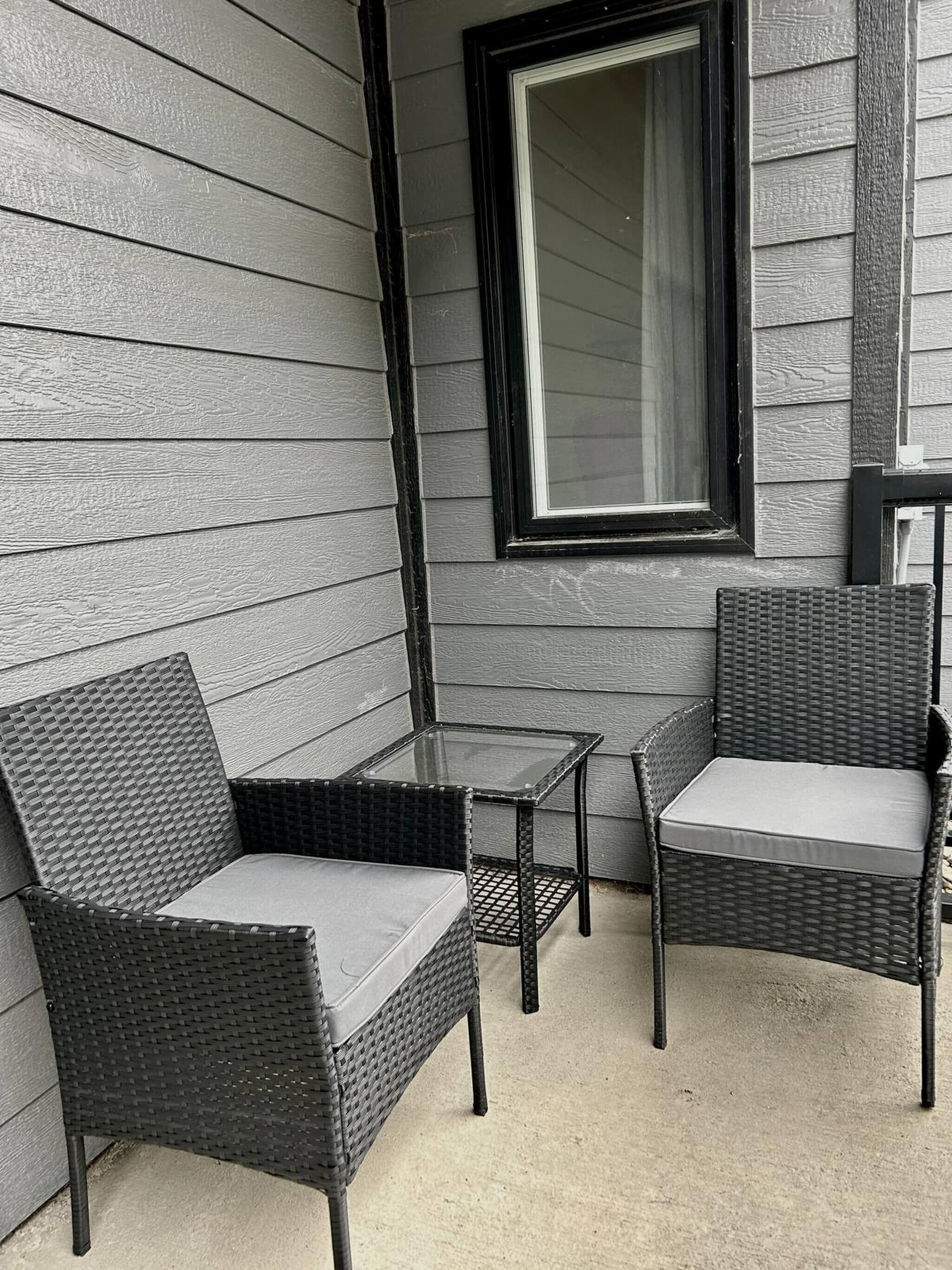 A patio area with two wicker chairs and a small glass table, adjacent to a window with a black frame.