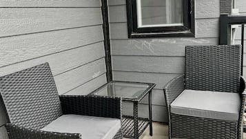 A patio area with two wicker chairs and a small glass table, adjacent to a window with a black frame.