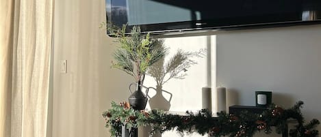 A living room with a flat-screen TV mounted on the wall, a Christmas garland, two wicker baskets, and a large window with curtains.