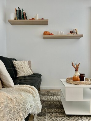 A modern living room with a black sofa, white throw blanket, and a white coffee table with decorative items.