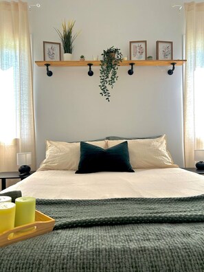 A neatly made bed with a dark green pillow, a bedside table with a lamp, and a tray with candles. - Beautiful Park Side Apartment (Steinbach)