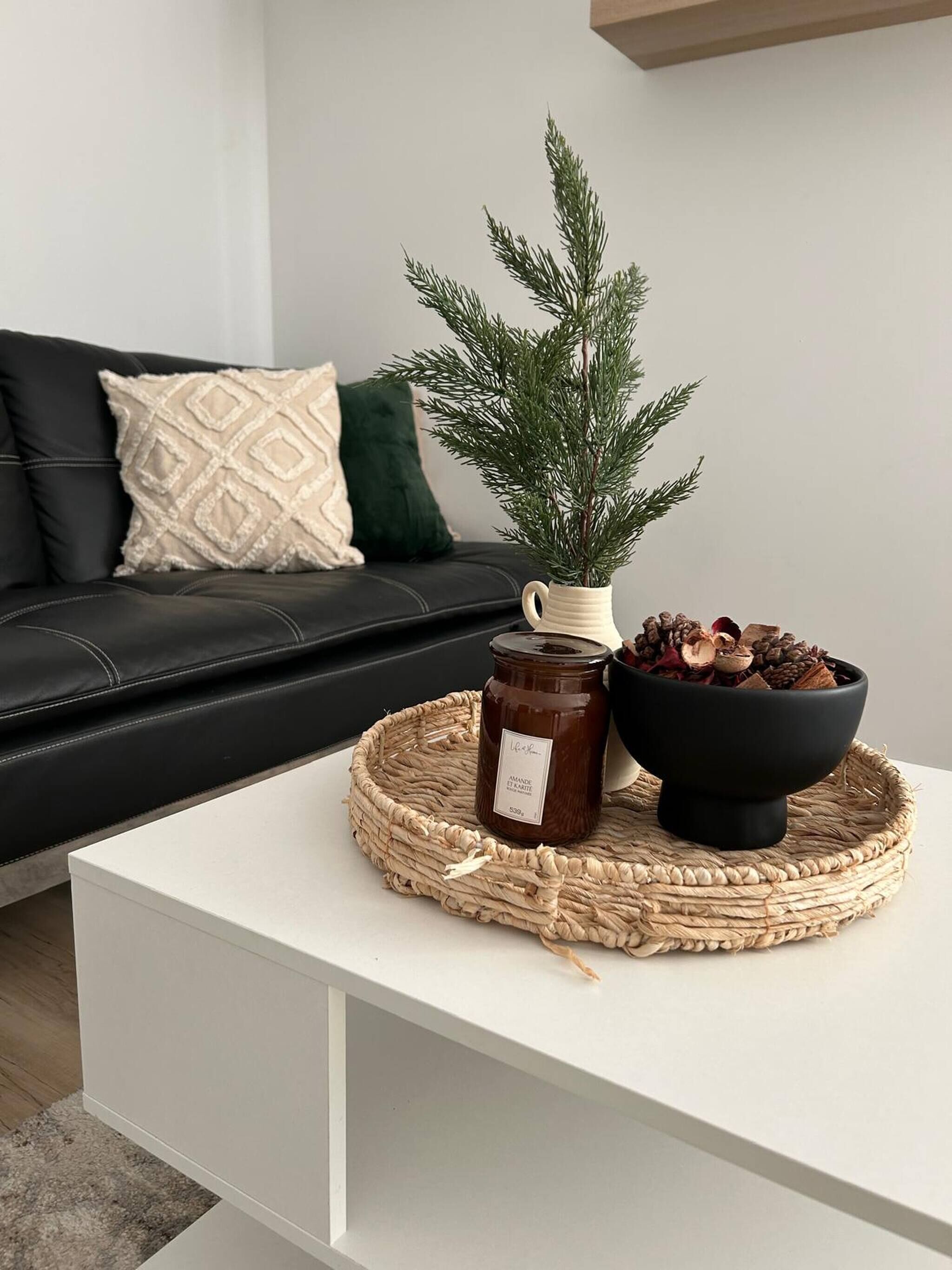 A modern living room with a white coffee table, a decorative pine branch, a jar of honey, and a bowl of pinecones.