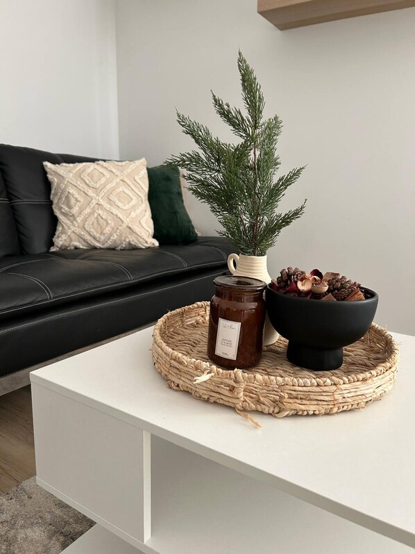 A modern living room with a white coffee table, a decorative pine branch, a jar of honey, and a bowl of pinecones.