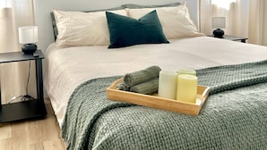 A neatly arranged bedroom with a bed, bedside tables, a tray with towels and candles, and a wall-mounted shelf with plants and pictures. - Beautiful Park Side Apartment (Steinbach)