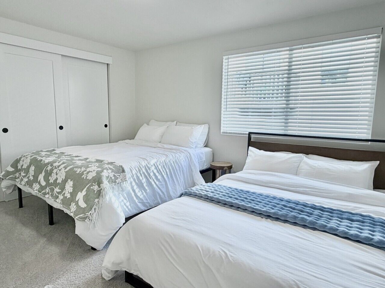 A bedroom with two beds, a closet, and a window with blinds.