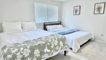 Un dormitorio con dos camas, una ventana con persianas y dos cuadros en la pared.