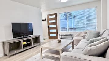 Una sala de estar con televisor, sofá, mesa de centro y una puerta con ventanal.