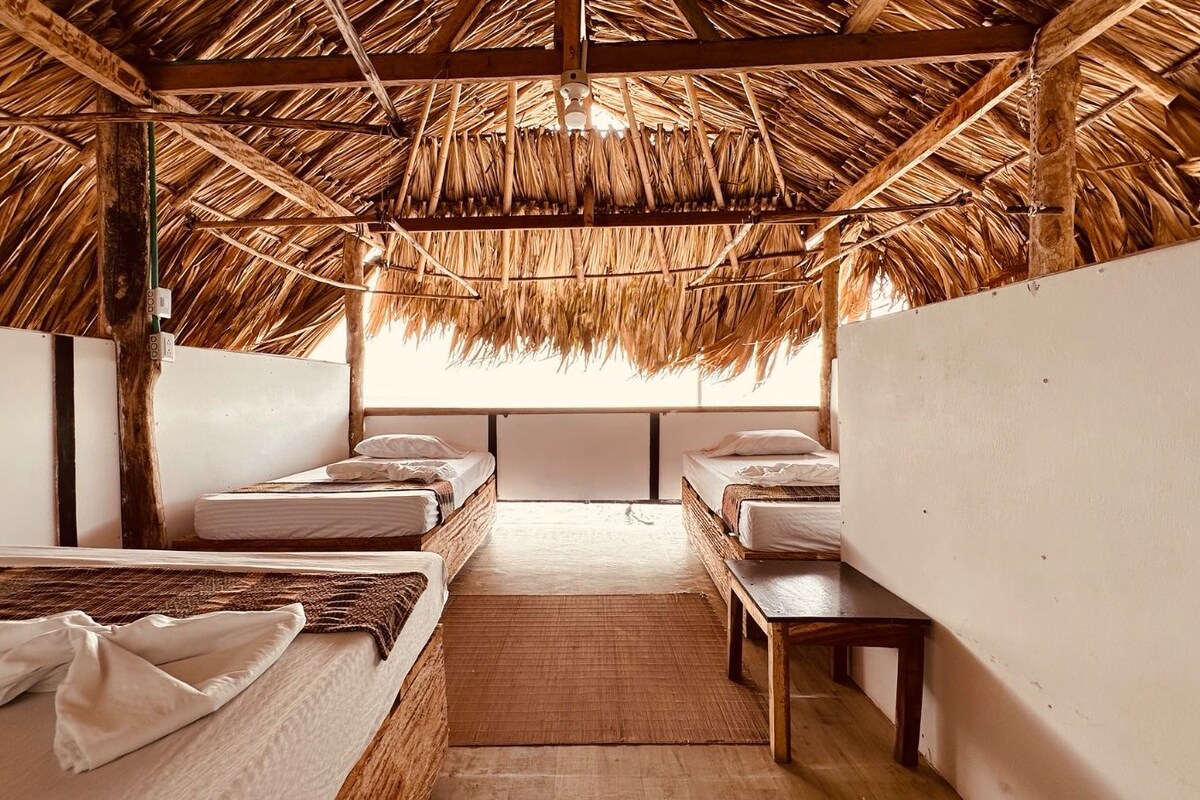A room with thatched ceilings, wooden beds, and a central bench.