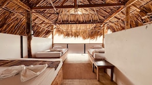 A room with thatched ceilings, wooden beds, and a central bench. - El Rincon de Juan (san onofre)