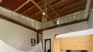 Quarto com beliche de madeira, uma cama de solteiro com mosquiteiro e ventilador de teto.
