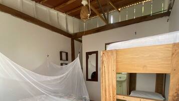 Una habitación con una cama litera de madera, una cama individual con mosquitera y un ventilador de techo.