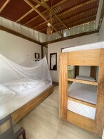Una habitación con una cama litera de madera, una cama individual con mosquitera y un ventilador de techo.