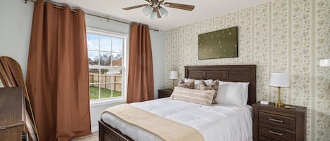 A bedroom with a wooden bed, two bedside tables with lamps, a ceiling fan, and a window with curtains.