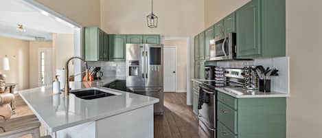 A modern kitchen with green cabinets, stainless steel appliances, and a central island with a sink.