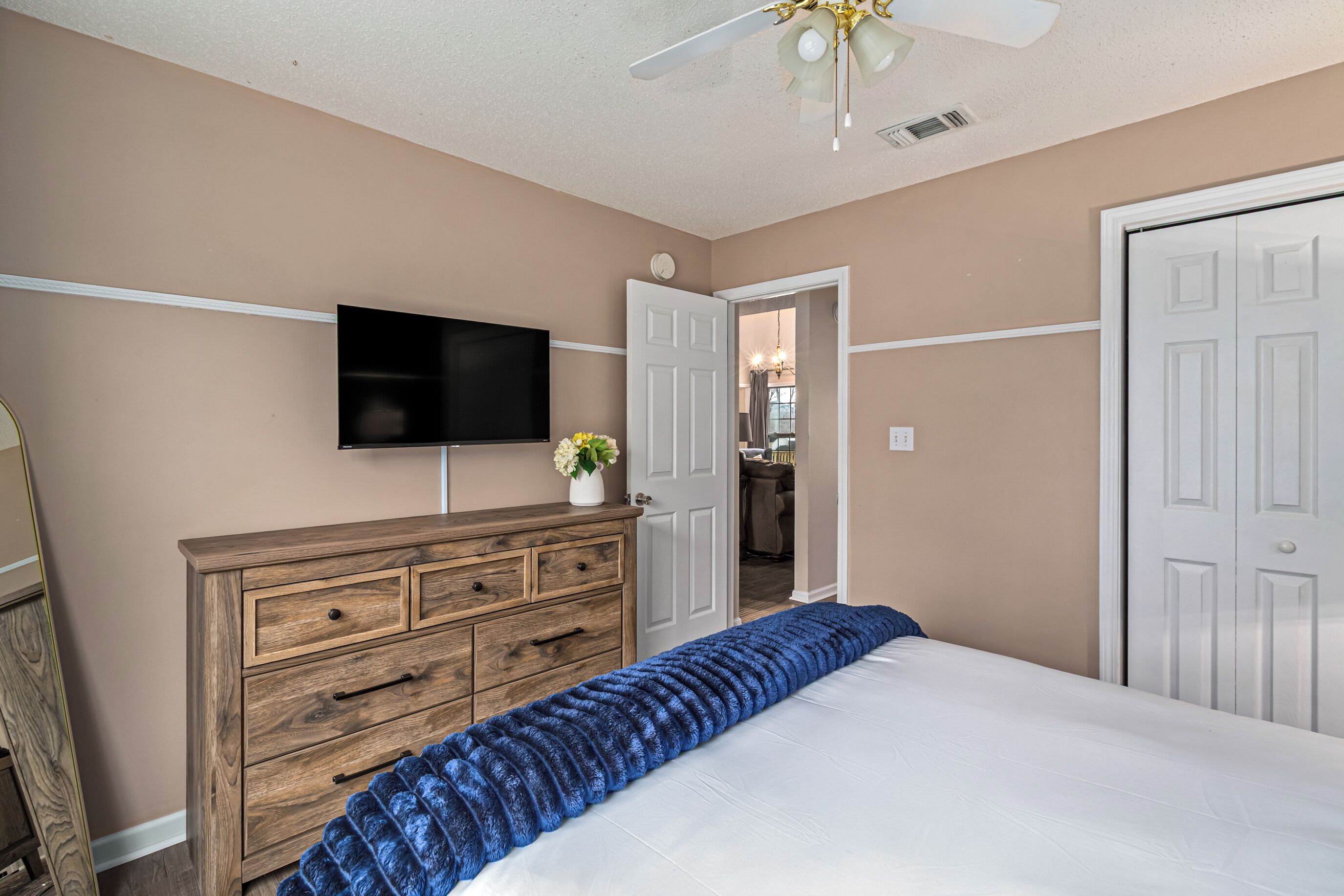 Un dormitorio con cama, cómoda, televisor y una puerta que da a otra habitación.