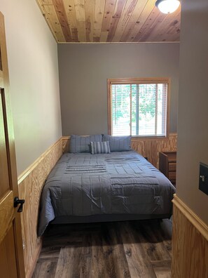A bedroom with a bed, wooden walls, a window, and a door. - Private and quiet retreat ,three blocks to the paved bike trail, (Deerwood)