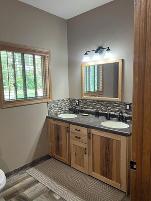 A bathroom with a double sink vanity, wooden cabinets, a mirror, and a window with blinds. - Private and quiet retreat ,three blocks to the paved bike trail, (Deerwood)