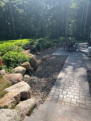 A paved patio with a seating area, surrounded by a garden with rocks and plants. - Private and quiet retreat ,three blocks to the paved bike trail, (Deerwood)