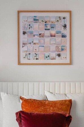 A framed collage of beach scenes on a wall above a bed with white and red pillows. - Boho Palms by Coastline Vacation Rentals (San Diego)