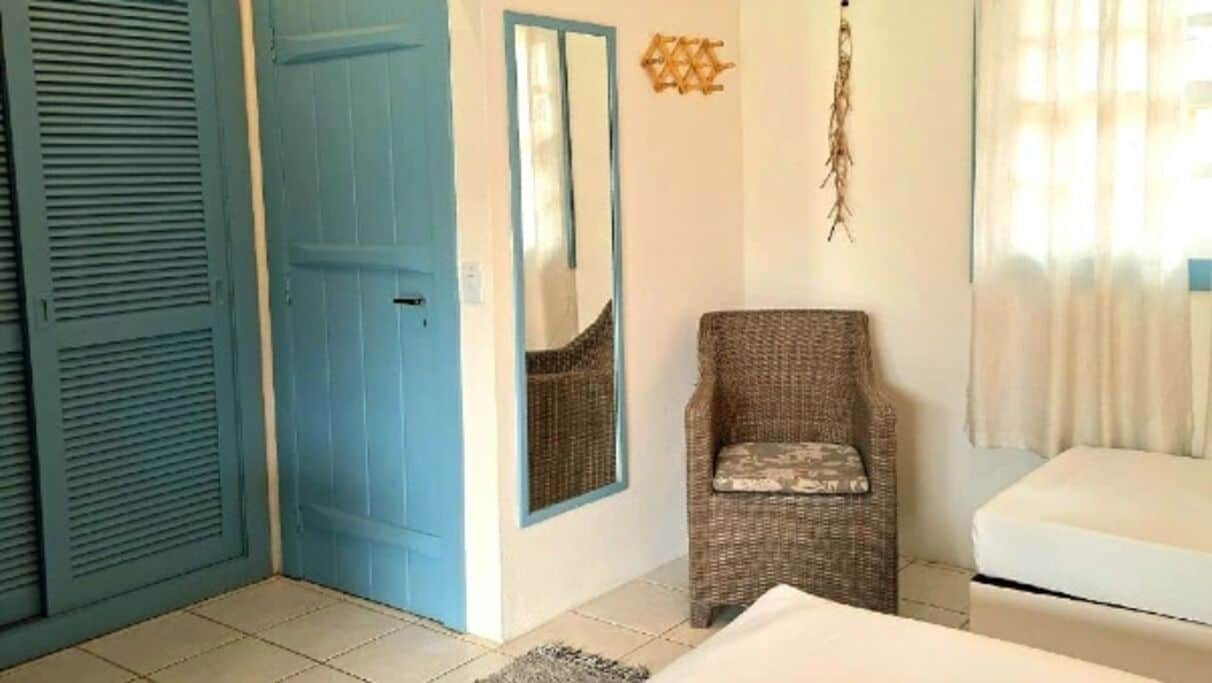 A room with a blue door, a wicker chair, a white sofa, and a mirror on the wall.
